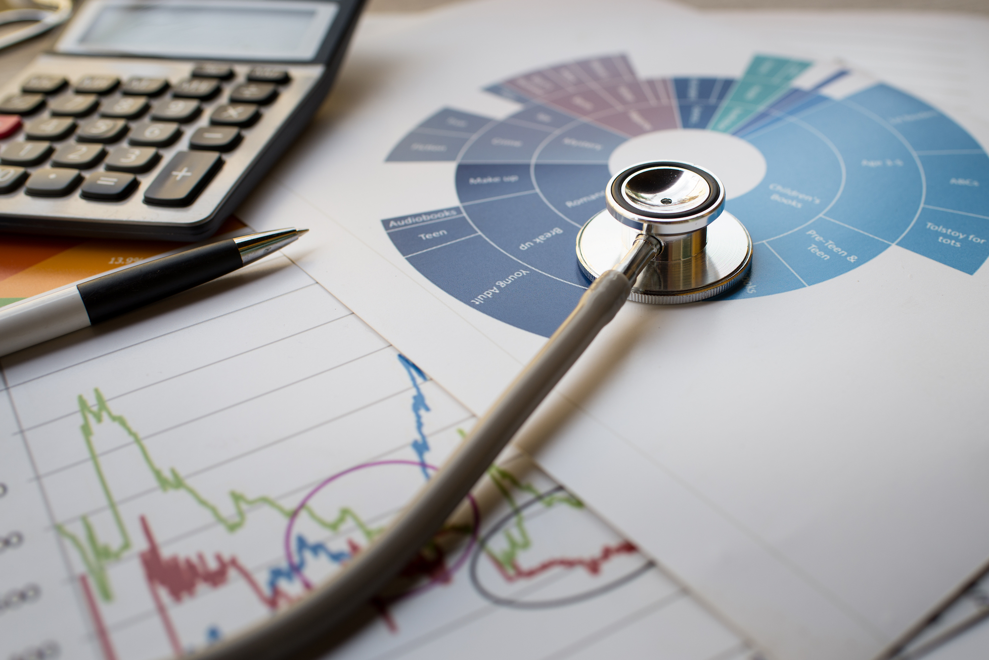 a desk with a calculator, pen, graphs and a stethoscope